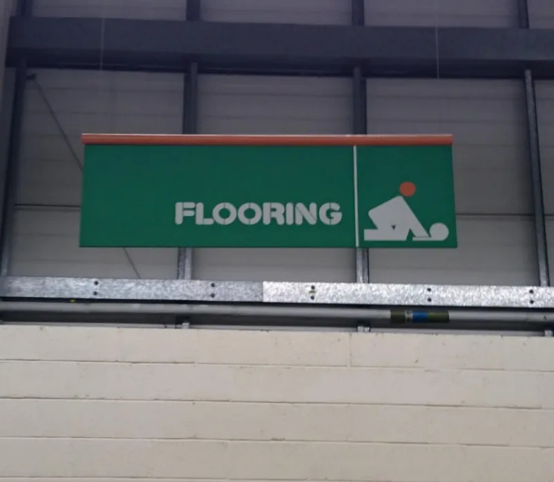 Muestra el cartel de la tienda "PAVIMENTOS" con un icono de una persona inclinada, que sugiere la instalación del suelo... o una pose de ******