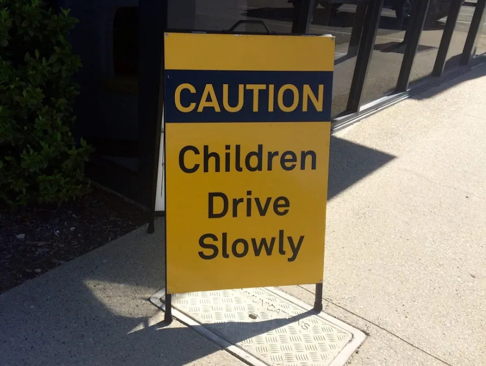El signo dice: "Precaución: los niños conducen lentamente."
