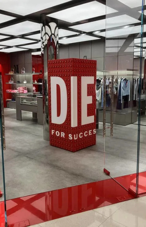 Interior de la tienda con lectura de carteles "MORIR POR EL ÉXITO" en letras grandes