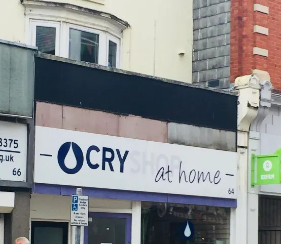 El cartel encima de una tienda dice "CryShop en casa," con un icono de gota de lluvia; sin embargo, el "tienda" está desvanecido, por lo que parece leerse "llorar en casa"