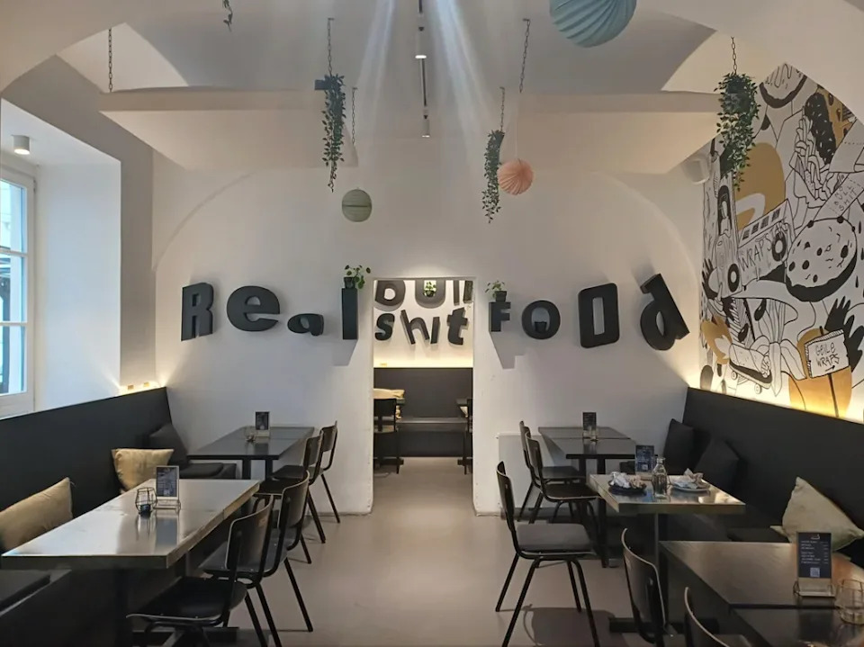 Interior del restaurante con letras grandes en la pared que leen "comida real;" ambas palabras están separadas por una puerta que muestra letras en la pared del fondo, haciendo que parezca leída "comida de verdad"