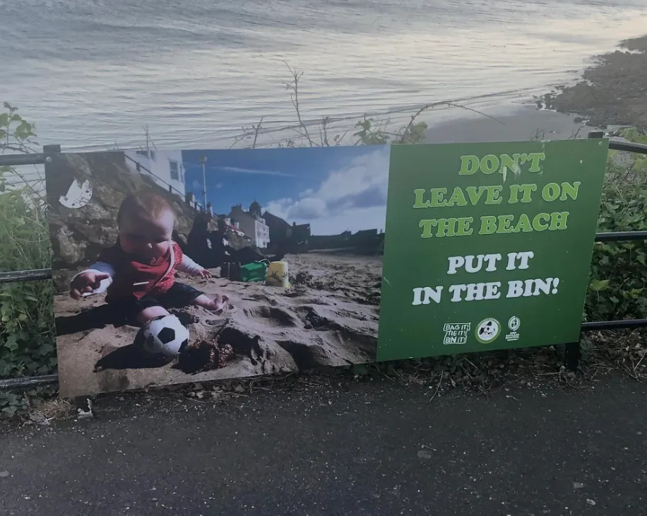 Un letrero en la playa muestra a un niño jugando con la basura, pidiendo a la gente, "No lo dejes en la playa. ¡Ponlo en la papelera!" No está claro si se refieren a la basura o al bebé